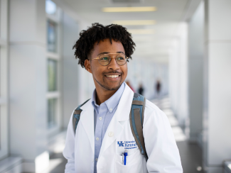 A male student posing for a picture while wearing a College of Medicine coat.