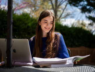 A female student studying outside with a laptop and books.