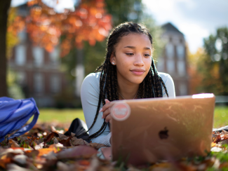 A female student outside looking at a laptop.