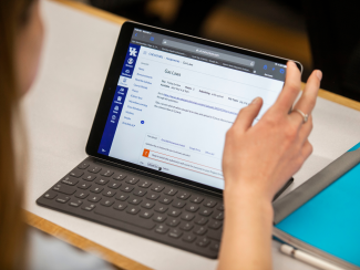 An iPad with keyboard displaying class information, the hand of a student in view on the right.