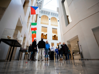 A small group of people standing in the W.T. Young Library underneath several nations flags.